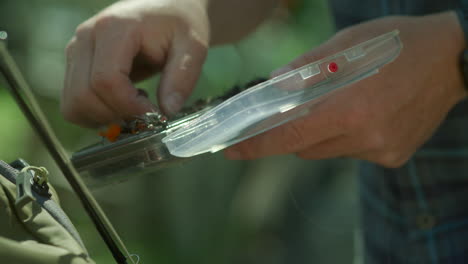 fly fisherman selecting fly from lure case in sun flares for flyfishing fishing