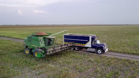 aerial - combine harvester maneuvers next to a truck, wide spinning shot