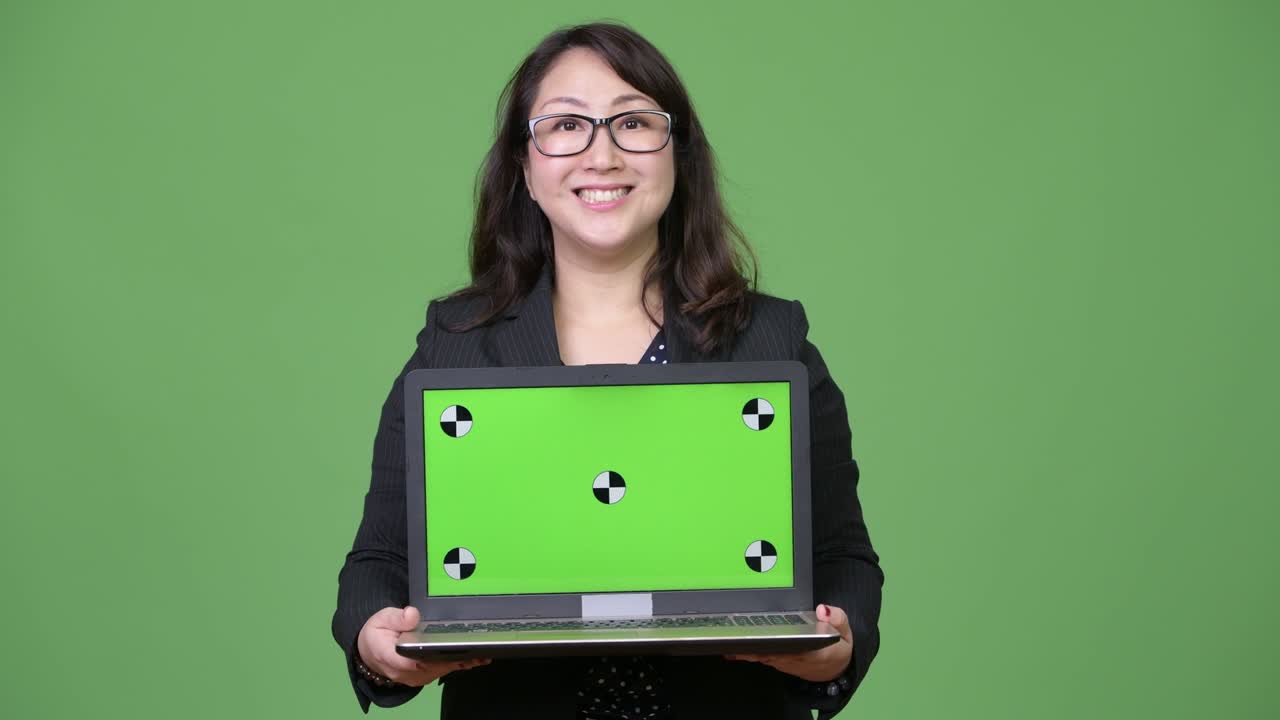 una hermosa mujer de negocios asiática madura mostrando una computadora portátil contra un fondo verde