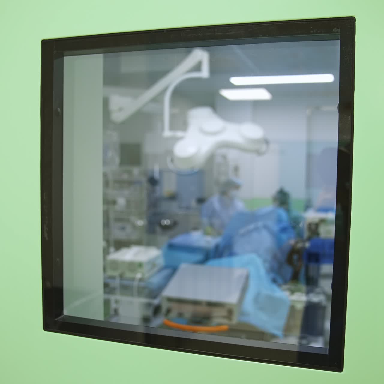 Looking through a little square window to a modern surgery room. Medics working in the operational theatre