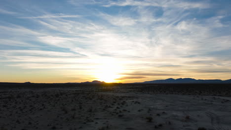 Hiperlapso-Aéreo-Rápido-Sobre-La-Silueta-Del-Desierto-De-Mojave-Durante-Una-Puesta-De-Sol-Dorada-Con-Un-Tenue-Paisaje-Nublado