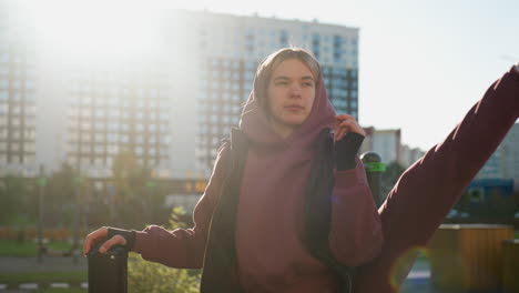 fit lifestyle advocate holds pull up bar while stretching side leg high in urban outdoor park under bright sun, hoodie outfit, resilience and flexibility highlighted during dynamic fitness session