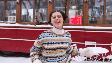 happy woman in winter clothes laughing in snowy street cafe