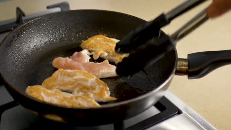 Close-up-slow-motion-shot-cooking-raw-chicken-in-kitchen-gas-top-cooker-stove-using-tongs-health-nutrition-hospitality-cooking-4K