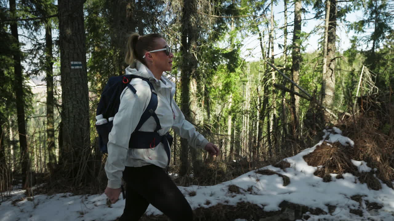 Pan shot of caucasian blond woman hiking in a forest during the day, gimbal shot