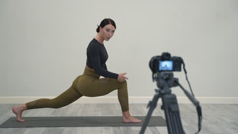 yoga at home. woman explaining warrior pose (virabhadrasana), recording a video tutorial, looking at a camera