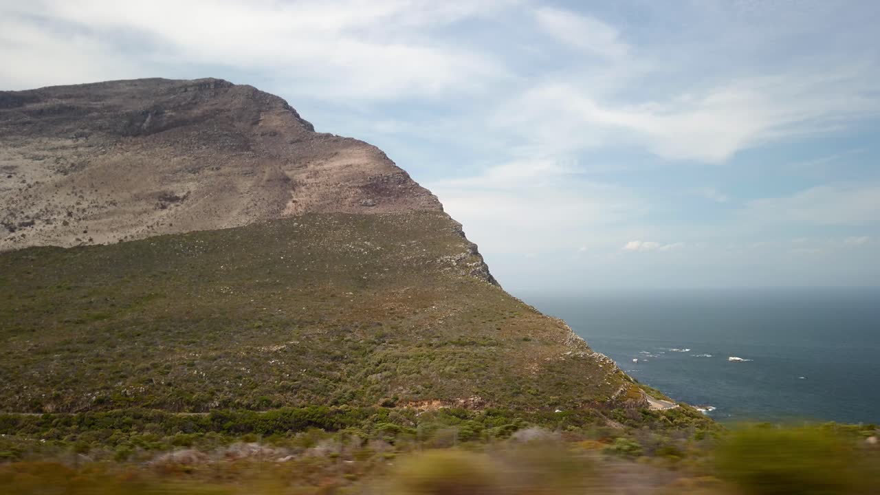 Vista panoramica dal finestrino dell'auto sul paesaggio costiero di scogliere e spiagge sudafricane del Capo di Buona Speranza, con skyline e formazioni geologiche