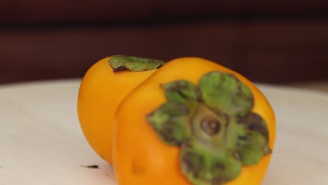 two persimmons resting on a wooden table