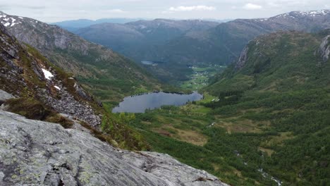 el lago de agua dulce leirovatnet y el pueblo de eidslandet en el fondo se revelan desde la cima de una montaña distante en stamnes vaksdal noruega - antena en movimiento hacia adelante cerca del acantilado y el punto de vista de la montaña