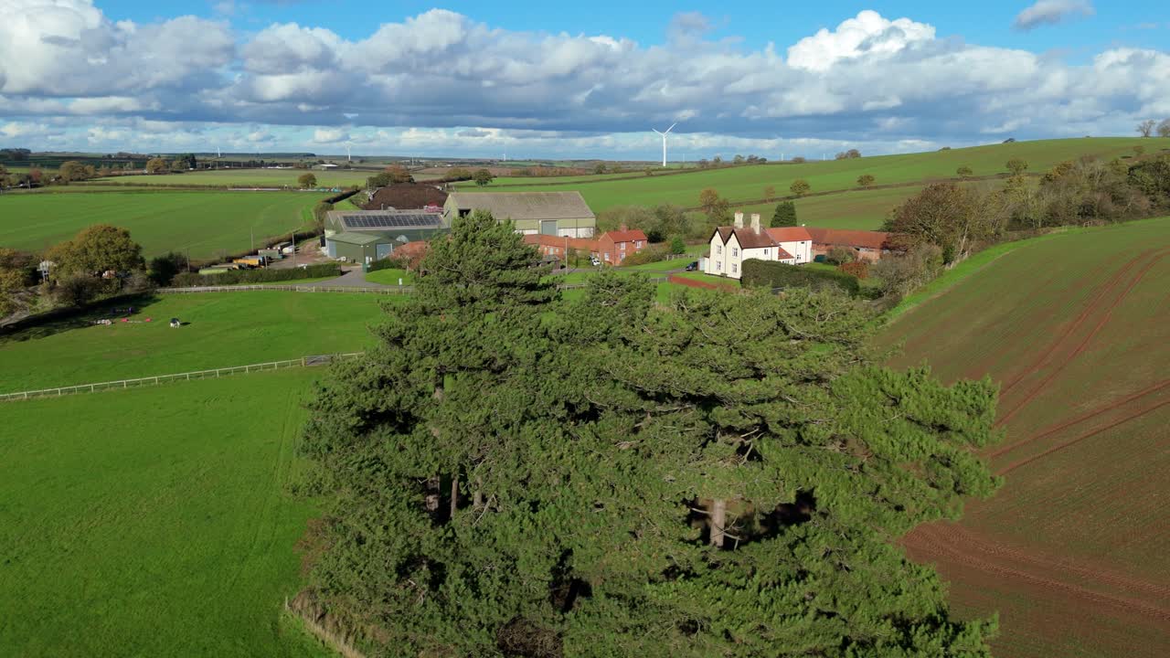 Vista aerea cinematografica con drone che rivela una piccola fattoria bianca e fienili circondati da un paesaggio rurale verde e soleggiato nel Nottinghamshire, Regno Unito