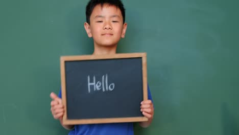 front view of asian schoolboy writing and showing text on slate chalkboard in classroom at school 4k