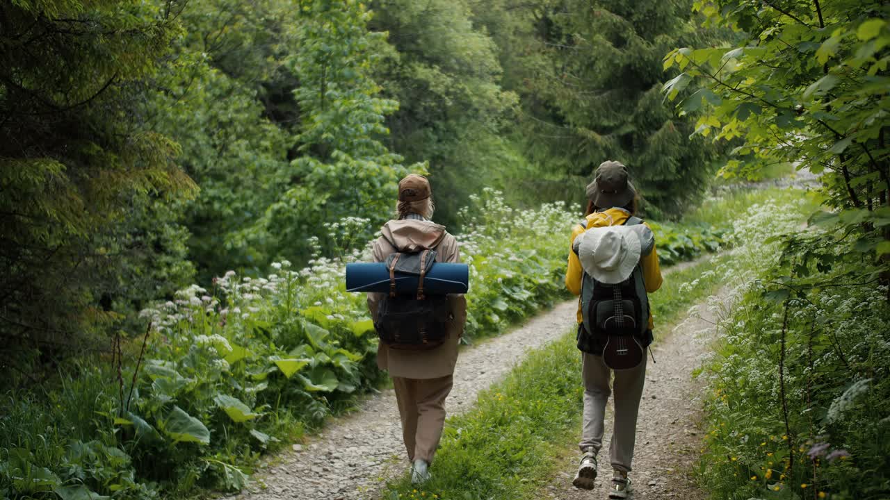 vista de atrás: dos niñas con ropa turística están caminando por la pendiente a lo largo del sendero con su perro. turistas caminan en el denso bosque verde