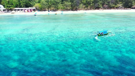 traditional balinese boat turning around in the crystal clear sea water near the white sandy beach