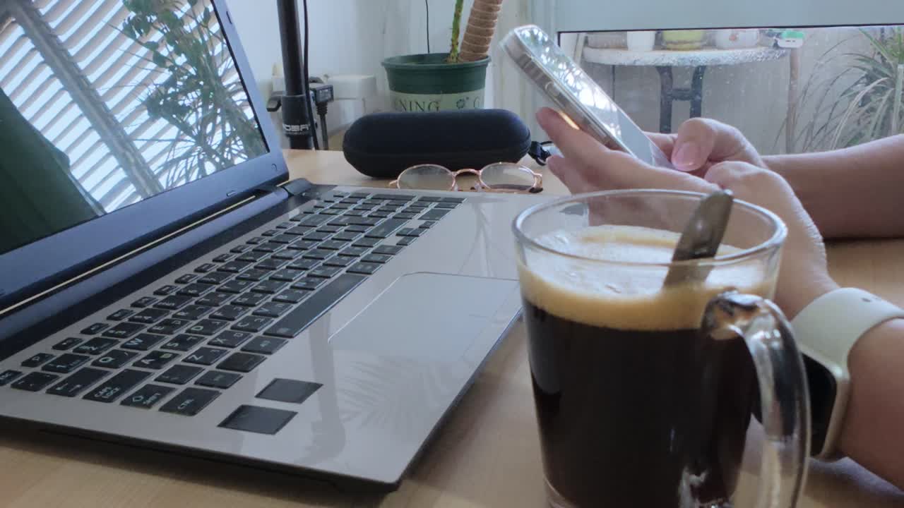 Relaxed moment at a desk with coffee, person casually browsing smartphone.