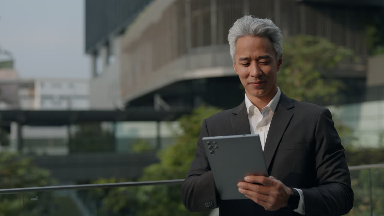 Smilende asiatisk forretningsmand med digital tablet udendørs