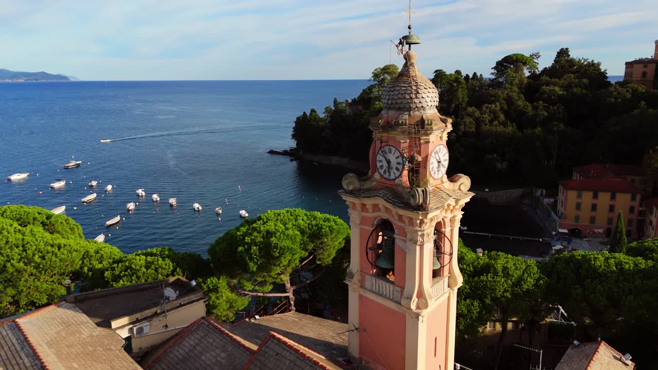 A picturesque shot of a traditional church bell tower in Liguria, Italy, captured on a clear sunny day. The tower stands tall against a vibrant blue sky