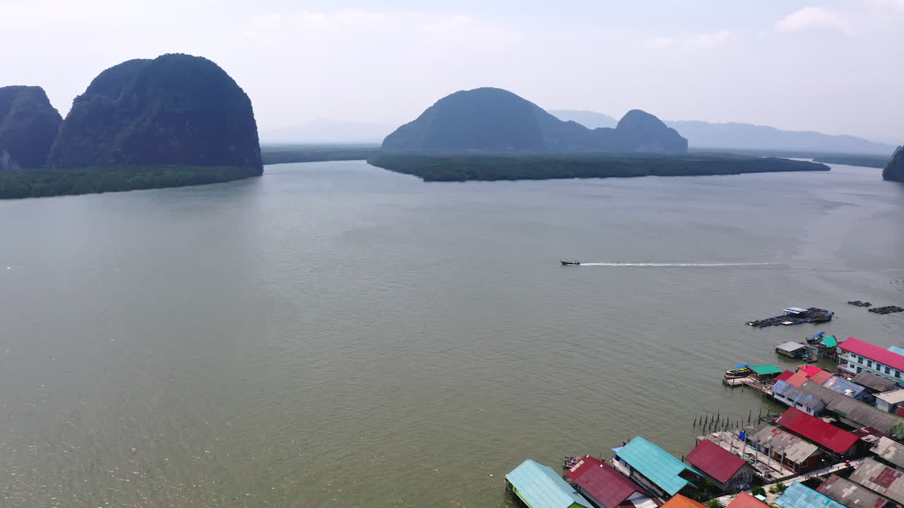 barco a motor navegando a lo largo de una aldea flotante en la bahía de phang nga, tailandia