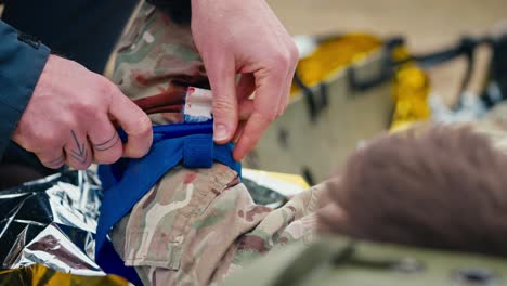 close up a confident male medic in a dark blue uniform puts a bandage on the wounded hand of a soldier to avoid blood loss during combat operations outside the city