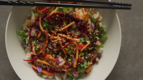 composition of bowl of stir fry noodels with chopsticks on grey background