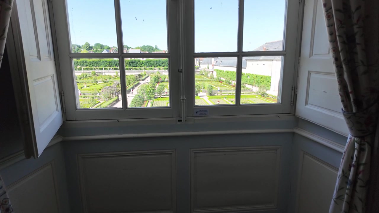 Ripresa lenta in avanti dalla stanza verso le finestre, che rivela gli iconici giardini rinascimentali del Castello di Villandry nella Valle della Loira, Francia
