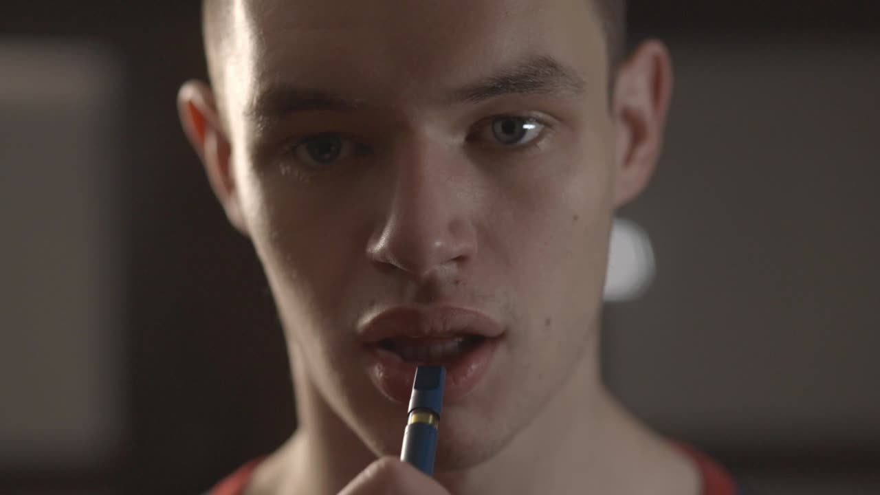 Young Caucasian Man Putting The Tip Of A Vape Pen On His Mouth. - Closeup Shot