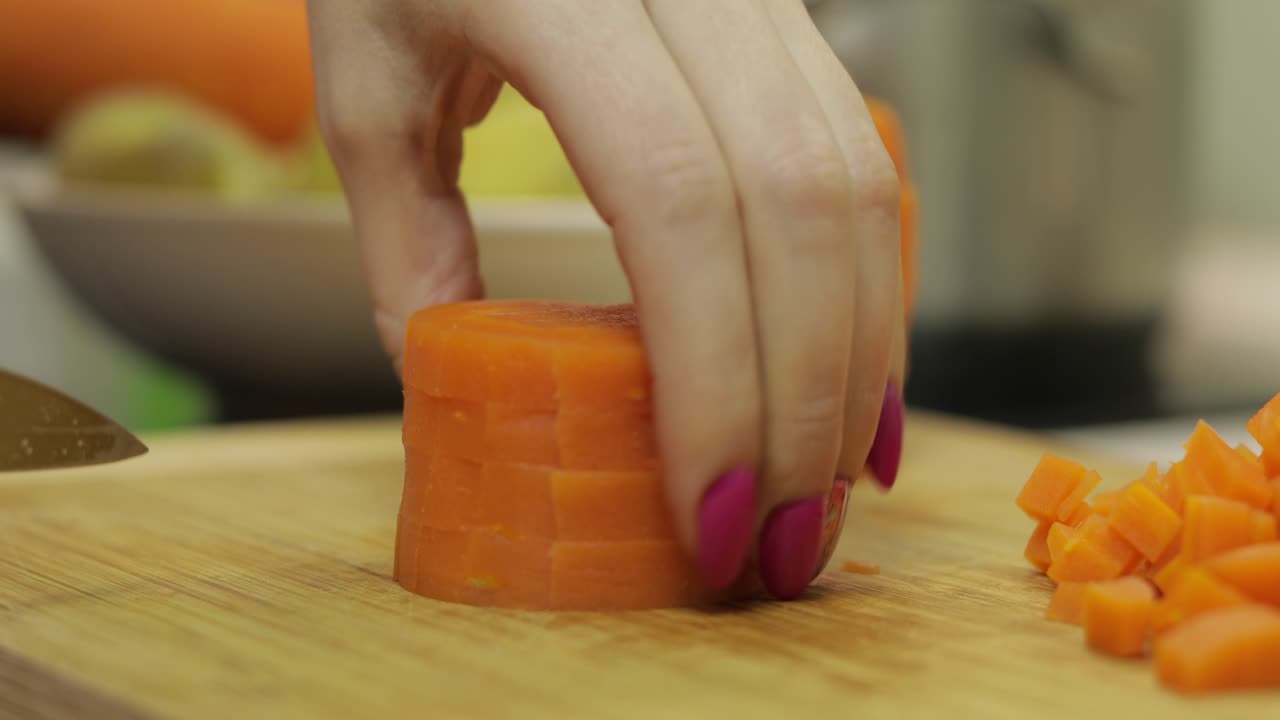 las manos de la ama de casa cortando zanahorias en pedazos en la cocina