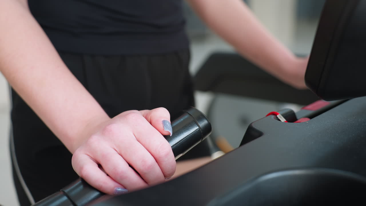 close up of girl wearing black shorts holding treadmill handle with painted fingernails during workout session in gym with blurred fitness background