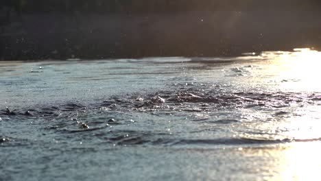 Zeitlupenaufnahmen-Von-Spritzern-Auf-Der-Wasseroberfläche-Vor-Einem-Hintergrund-Von-Sonnenuntergangslicht