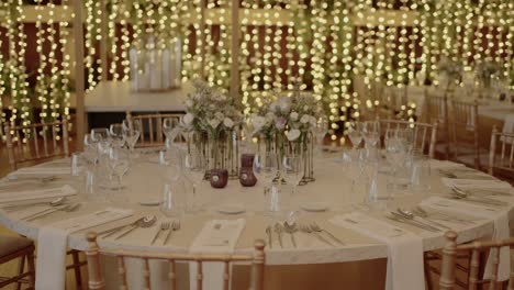 elegant wedding reception table setup with floral centerpieces and string lights in the background