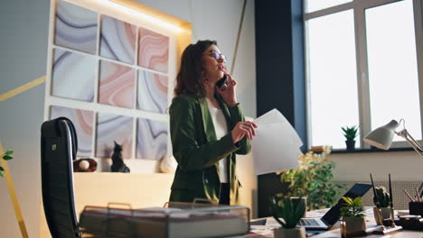 corporate worker talking cell phone standing modern office holding work papers.