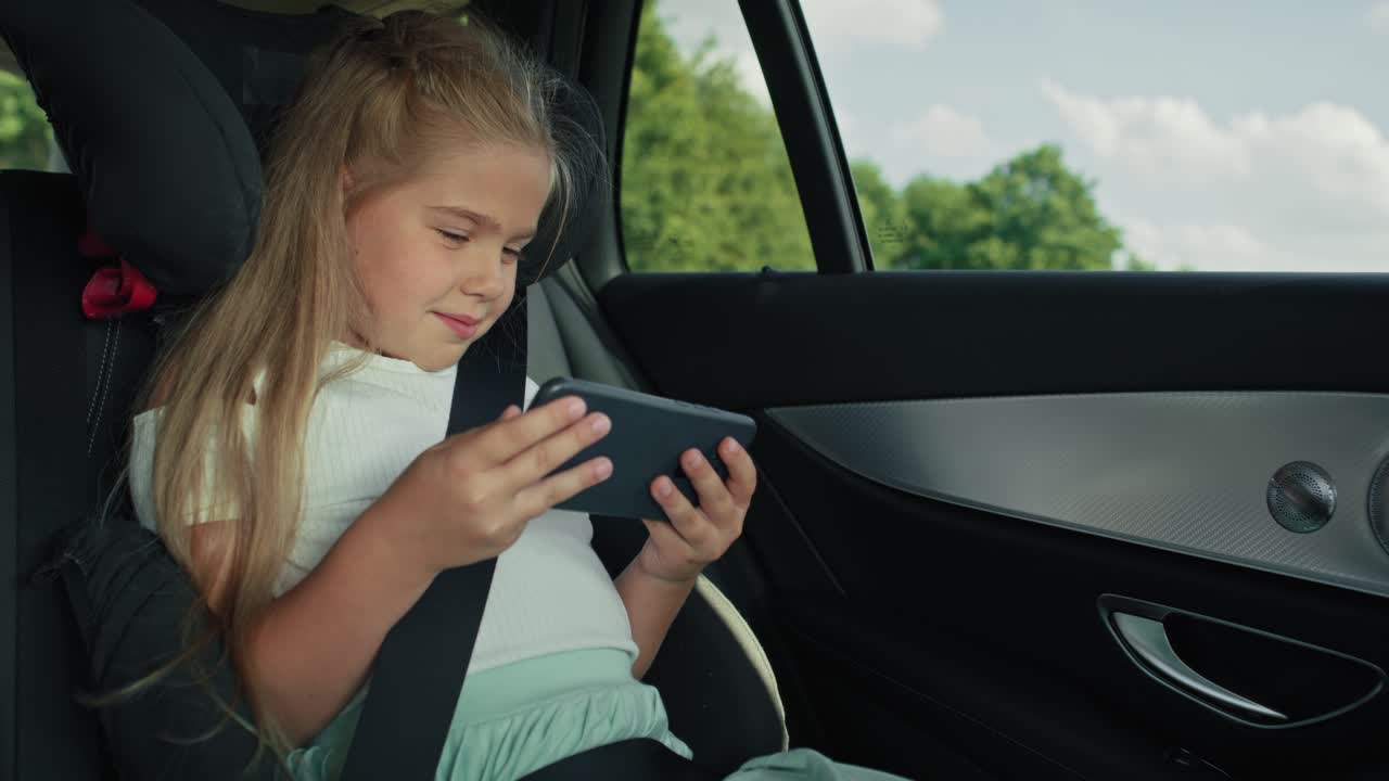 niña caucásica de 8 años usando teléfono móvil mientras viaja en coche.