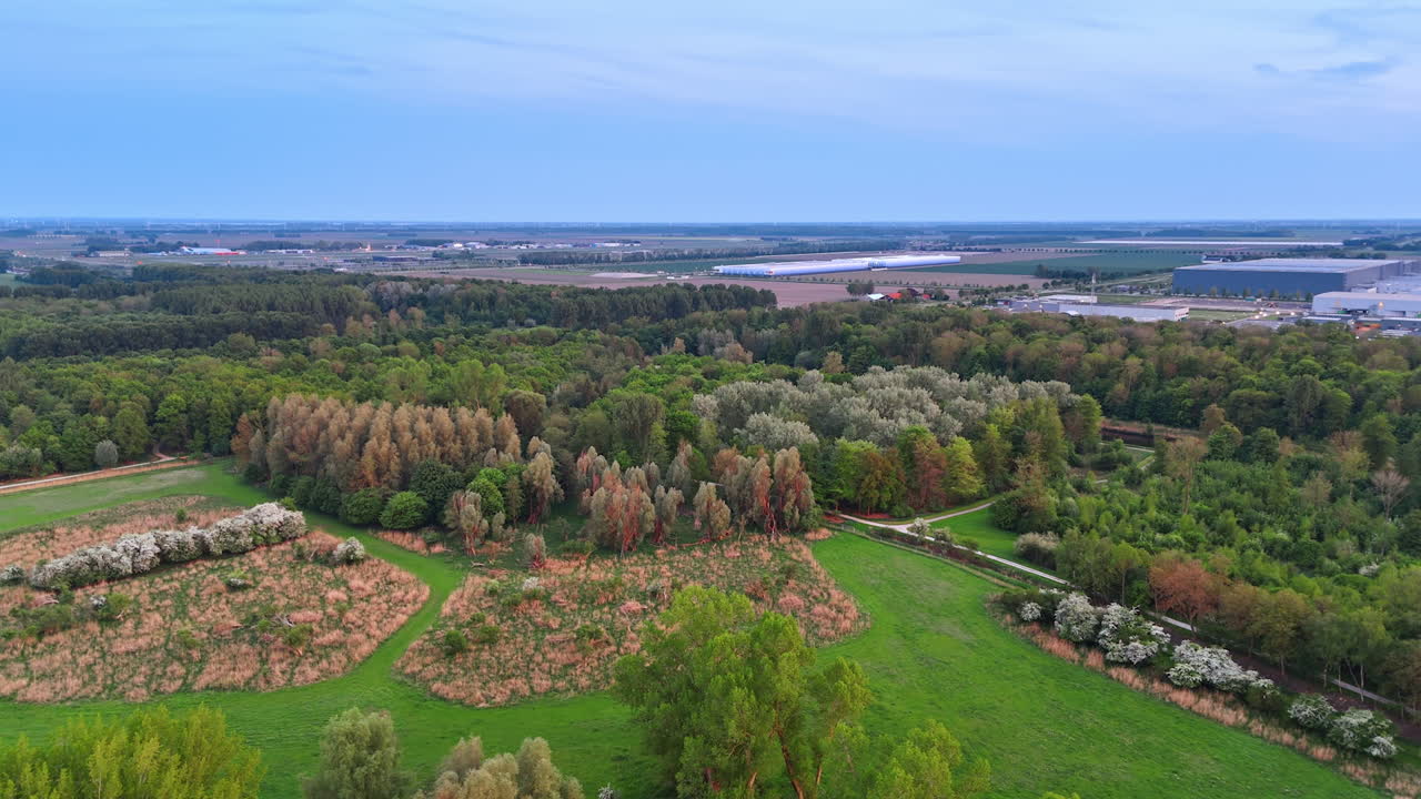 Green fields and trees. Aerial view of a green landscape with diverse trees, fields, and distant industrial structures