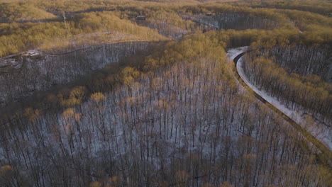 natchez trace scenic highway curves through scenic winter forest dusted in snow, aerial view at sunset