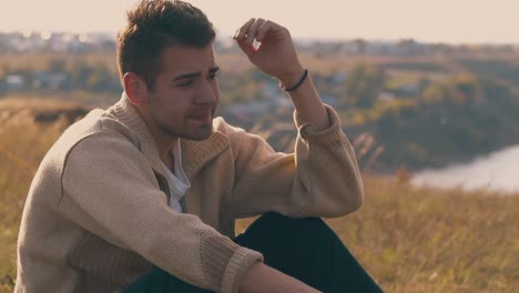 sad man in warm pullover sits on meadow lit by autumn sun