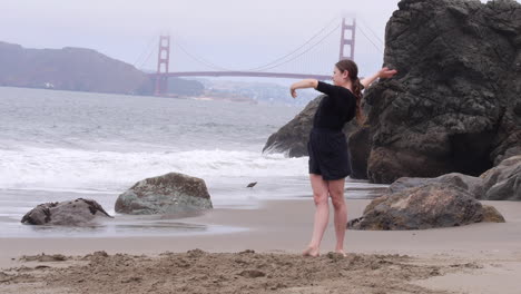Woman-Dancing-Barefoot,-Alone-on-Golden-Gate-Bridge-Beach-in-San-Francisco