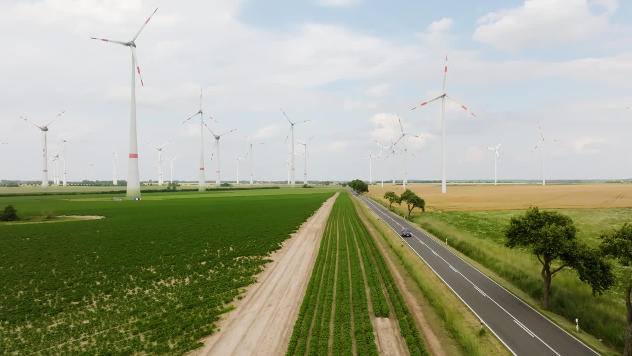Aerial view backwards over a farmland road and fields, in middle of wind farm