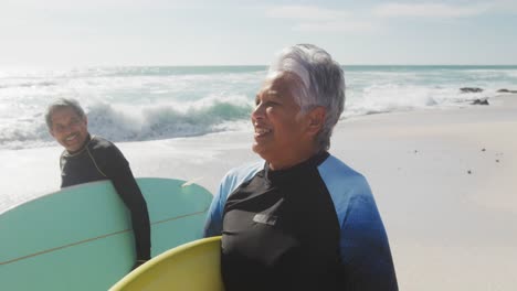 feliz pareja hispana senior caminando por la playa con tablas de surf