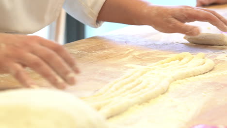 human-hand-modelling-and-making-piece-of-typical-tupe-of-italian-pasta-on-a-wood-table