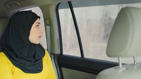 young muslim woman in hijab sitting in car on passenger rear seat. muslim woman day dreaming in back seat. a young woman in a hijab looks out the window.