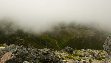 TimeLapse---Mist-flowing-into-valley,-shot-from-rocky-vantage-point-on-mountain-with-hiking-trails-in-background