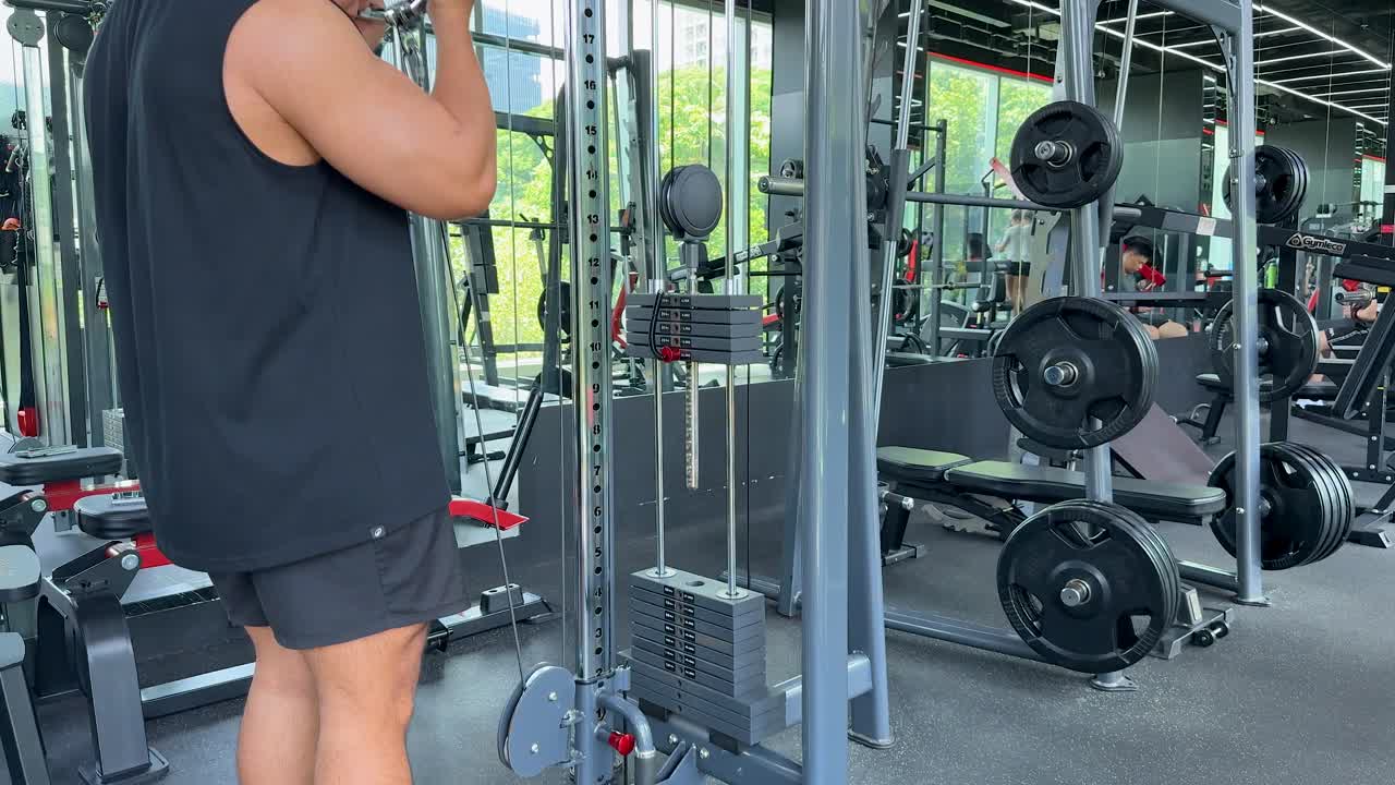 Athletic man performs standing cable bicep curls in modern, sunlit gym with mirrored walls