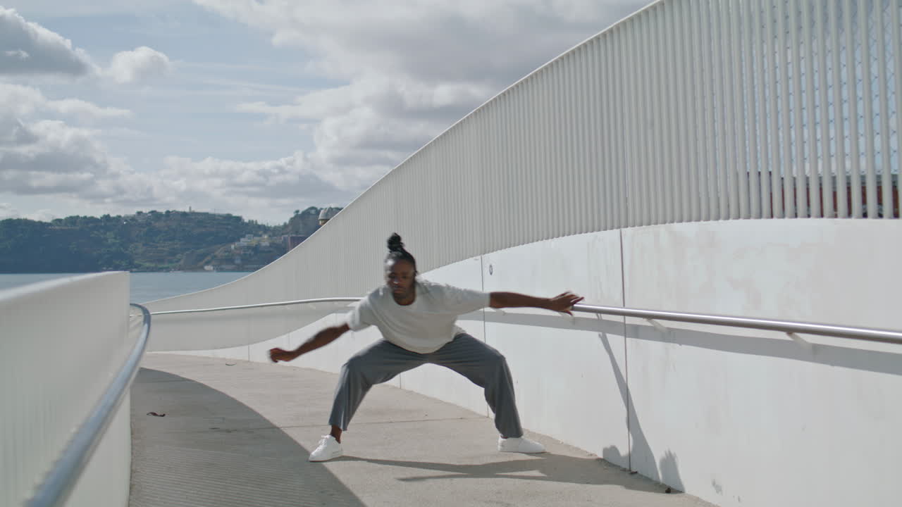 Dansende fyr optræder solo ved metalbro, vertikalt. Performer med brun hud danser.