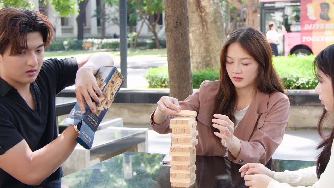 กลุ่มนักศึกษาไทยกำลังเล่นเกมต่อไม้บล็อกที่โต๊ะกลางแจ้งในบริเวณมหาวิทยาลัย