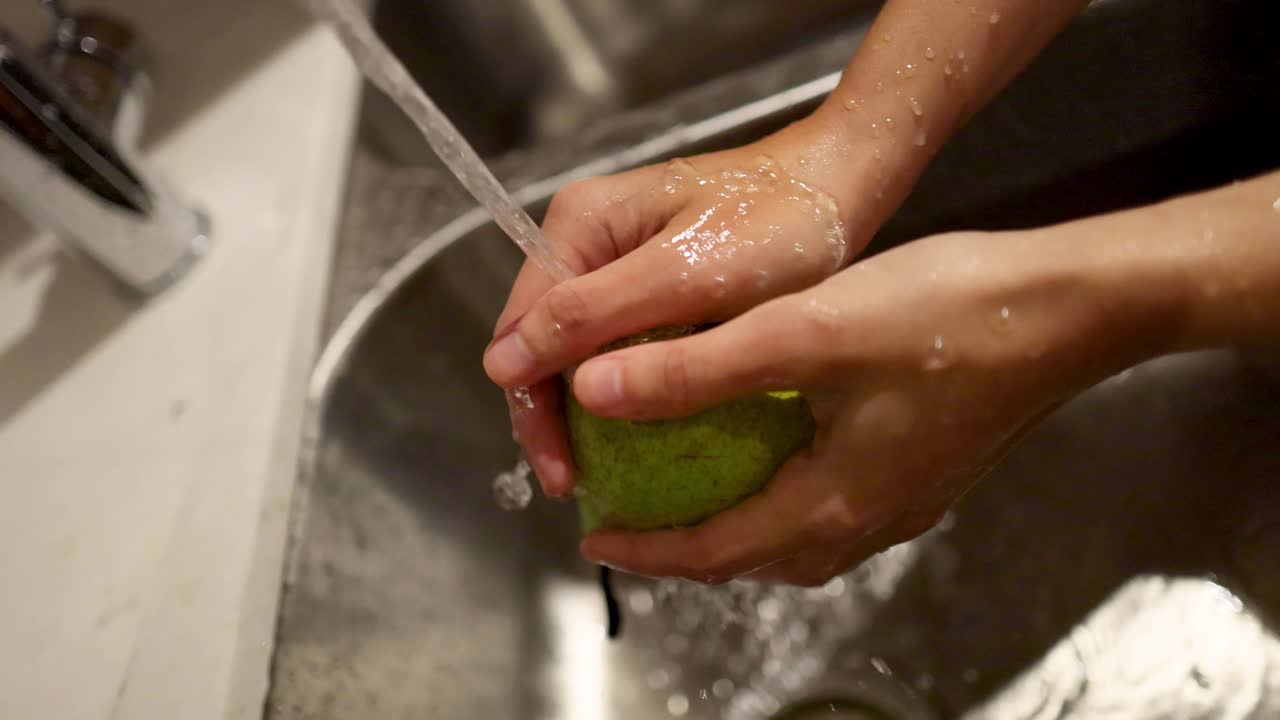 manos lavando una pera bajo agua corriente