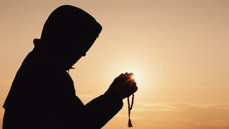 silhouette of a man in the hood sifting through the rosary at sunset