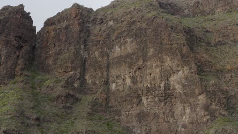 Intriguing-deep-orange-volcanic-rock-face-with-lush-green-growth-creeping-up-to-the-top