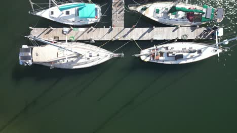 overhead drone footage of sailboats in marina tracking along dock