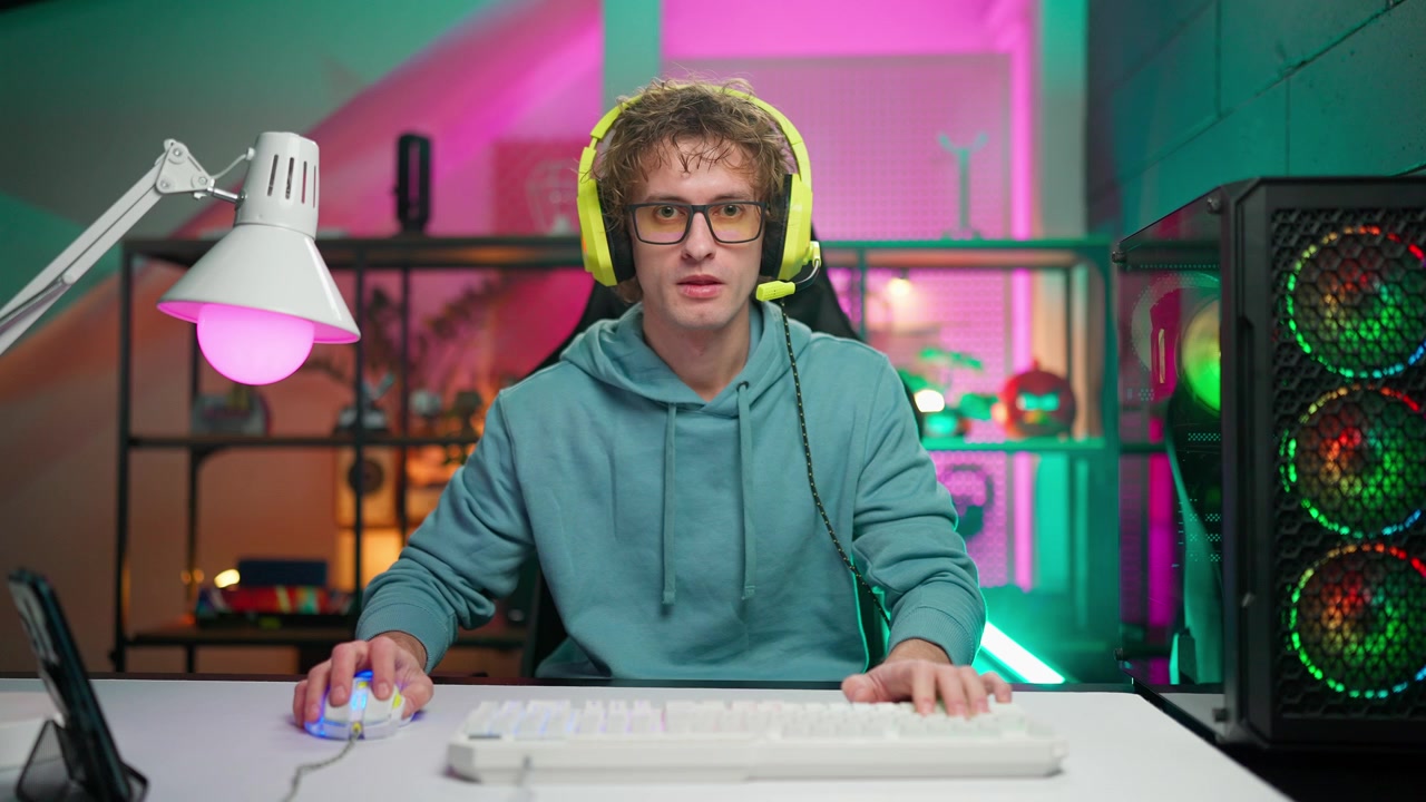 Junger männlicher Gamer mit Kopfhörern und Brille blickt in die Kamera