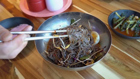 mezclando deliciosos fideos coreanos de trigo sarraceno con un par de palillos - super cerca