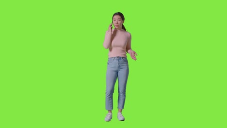 full length studio shot of frustrated woman answering call on mobile phone against green screen 1